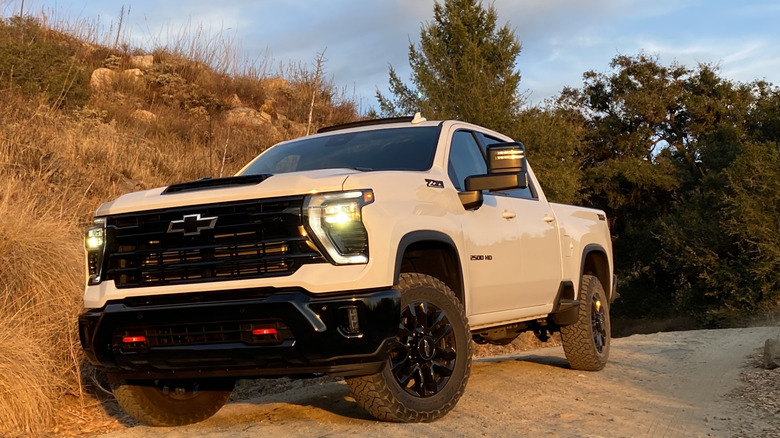 White Chevrolet Silverado 2500 HD Trail Boss parked on a dirt road in front of trees