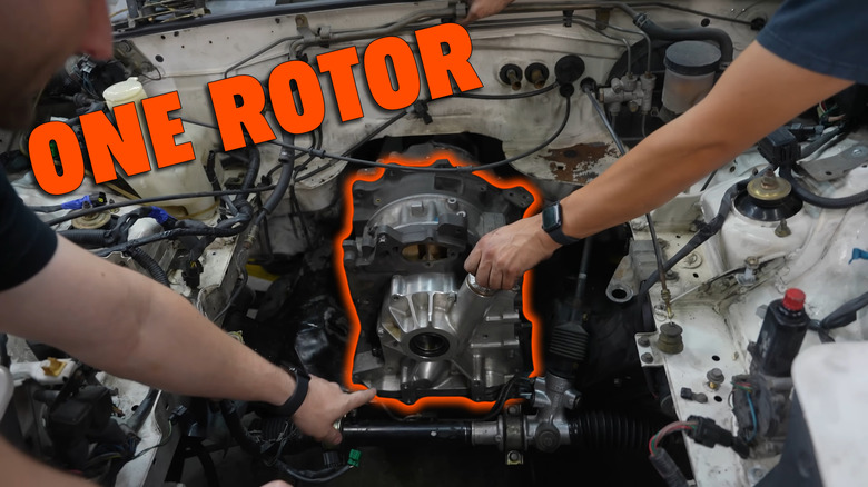 Two men hold a single-rotor engine into an engine bay