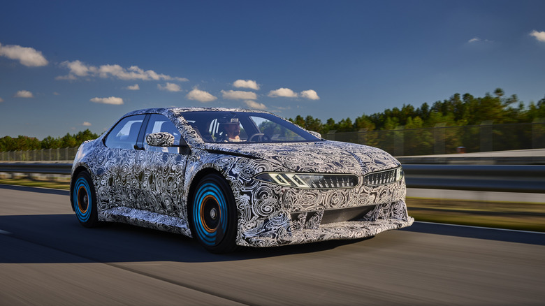 The Neue Klasse Vision Vehicle driving on a track covered in black and white camo with blue lights on its wheels