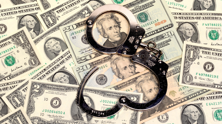 a pair of open handcuffs sitting on top of a pile of us dollars of assorted denominations