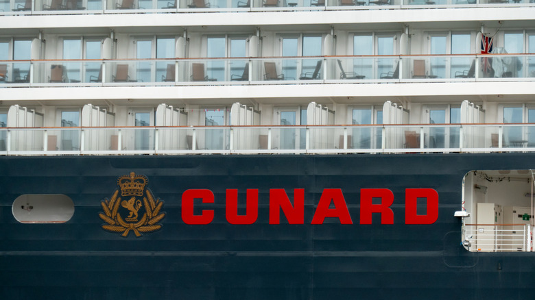 The hull and passenger balconies of the cruise ship, Queen Anne, docked at the Overseas Passenger Terminal at Circular Quay in Sydney Harbour. In the middle far right balcony, the flag of Great Britain is hanging om the wall. This image was taken from a public passenger ferry on a hot and sunny morning on 1 March 2025.