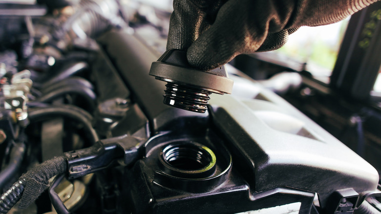 A photo of a hand unscrewing an engine oil cap.