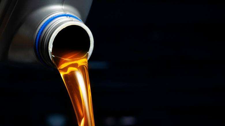 Engine oil being poured from a silver plastic bottle.