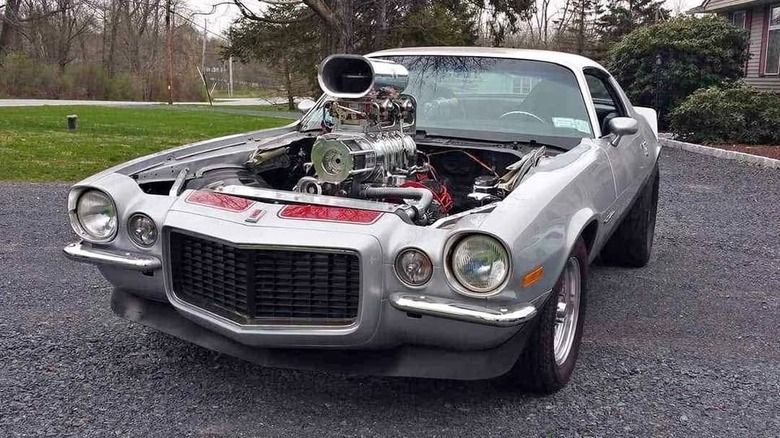 A silver Chevy Camaro with no hood and a blower out the top