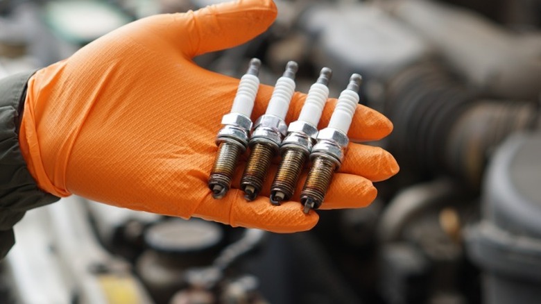 A person holding used spark plugs in their gloved hand