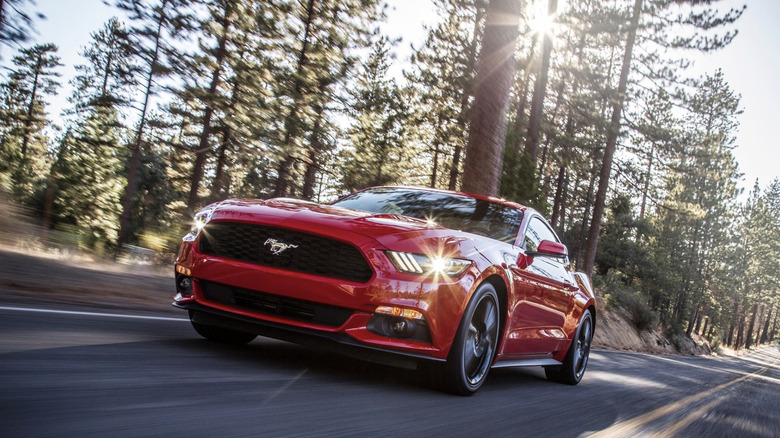 A red Ford Mustang driving in front of redwood trees