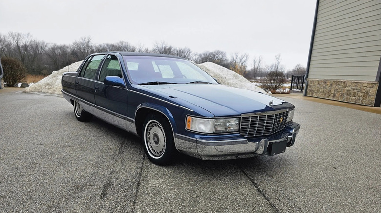 an immaculate navy blue 1996 cadillac fleetwood parked in front of a pile of snow