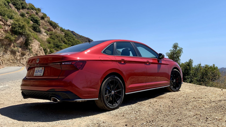 A red VW Jetta GLI parked on dirt in front of a mountain view