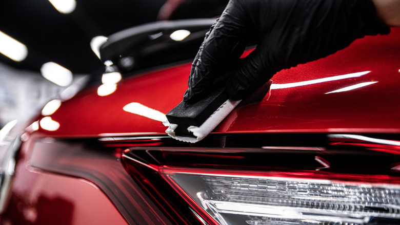 Car detailing studio worker applying ceramic coating on red car.