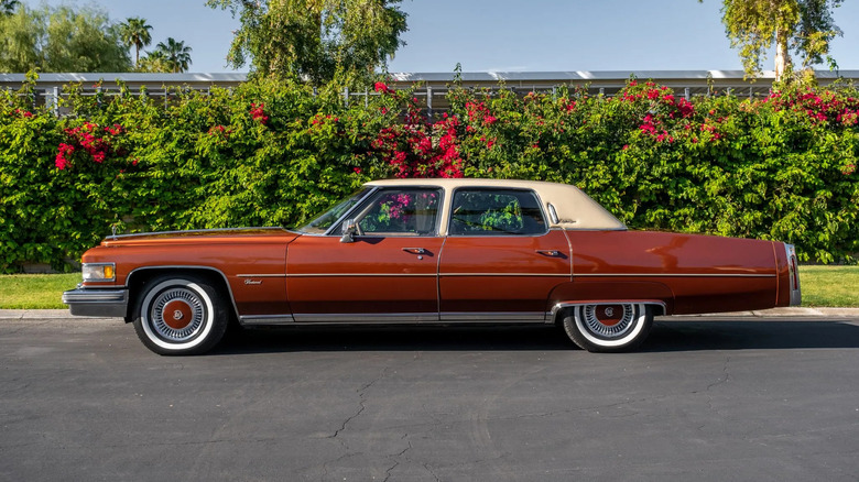 A side view of a brown Cadillac Fleetwood Brougham parked in front of bushes