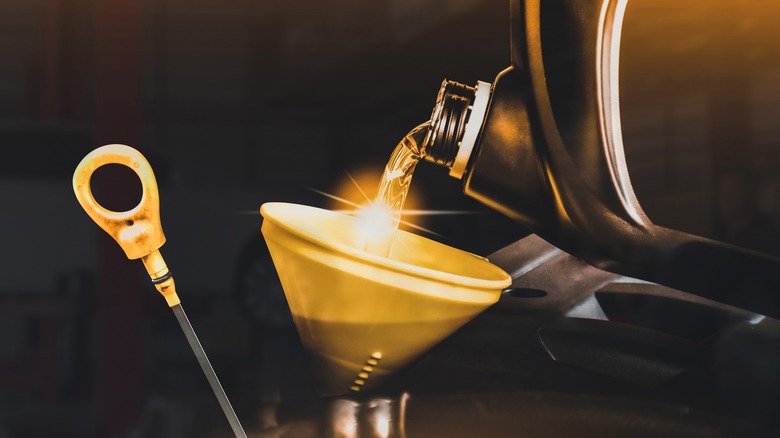 Oil being poured from a large jug into a yellow funnel during an oil change.