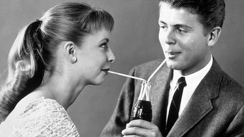 a photo of two people drinking from a bottle of coke.