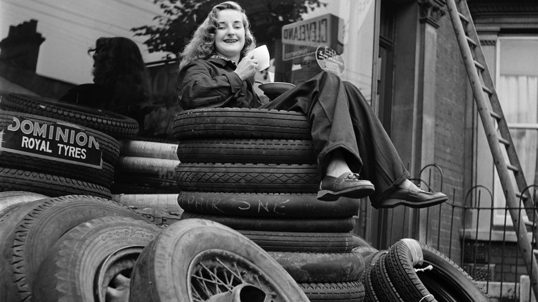 A vintage photo of a woman sitting on top of a pile of tires drinking tea