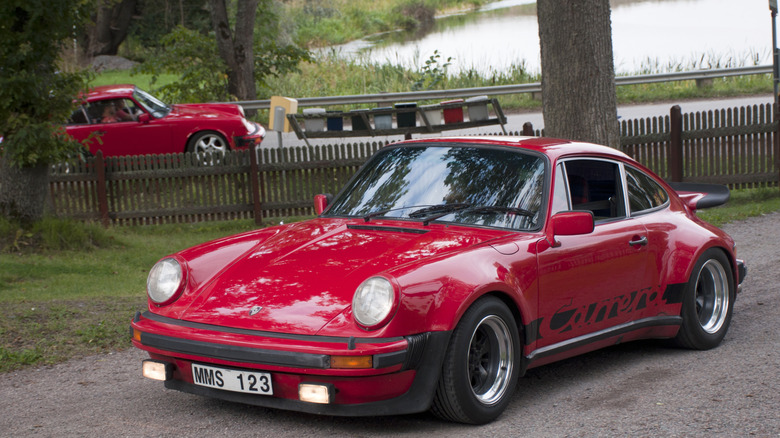 a red 77 Porsche 911 Carrera parked on dirt