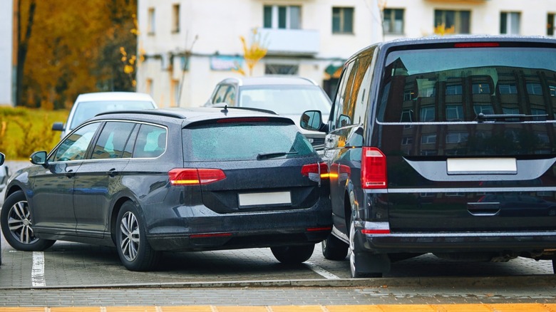 Car accident in tight parking lot, black sedan hitting parked van while backing up, reverse parking. Parking accident due to limited visibility, distracted driving. Rear-up collision. Minor accident  b