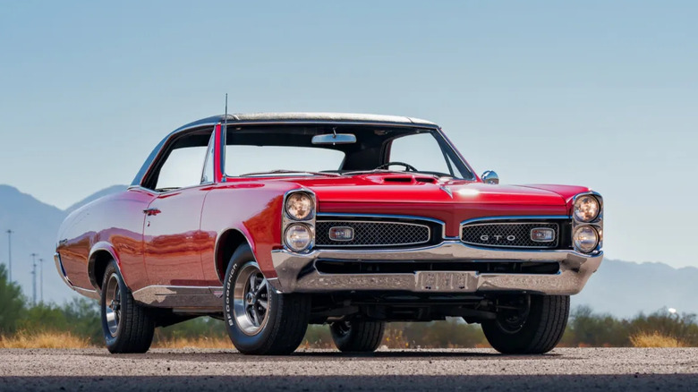 a red pontiac GTO parked in front of mountains