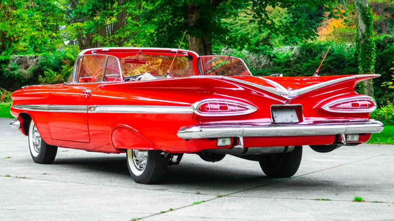 Rear three quarters of a red '59 Impala convertible in front of trees