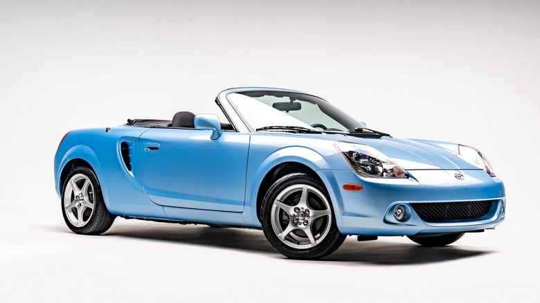 a light blue MR2 spyder parked in a studio with its top down