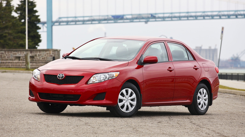 a red corolla parked in front of a bridge