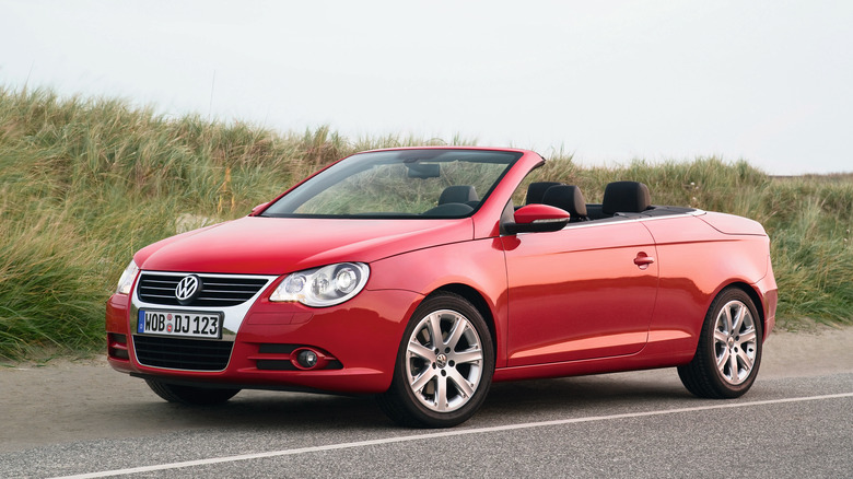 a topless red VW Eos parked in front of grass