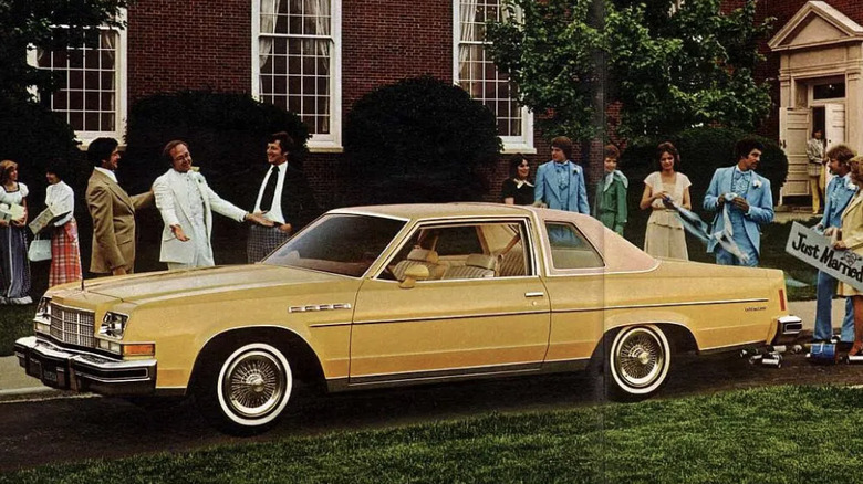 A picture of people gathered around a 1977 buick elantra