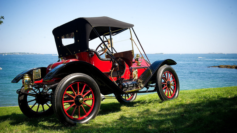 A red and black 1910 Oakland parked on a hill overlooking the sea.