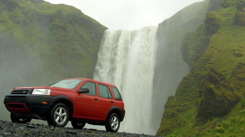 A photo of a Land Rover Freelander at the base of a waterfall.