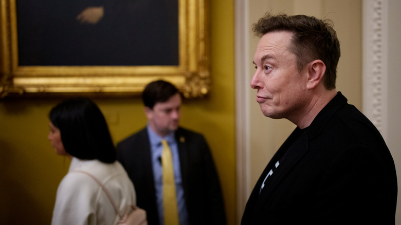 Elon Musk slouching in the White House while wearing a suit jacket and a t-shirt