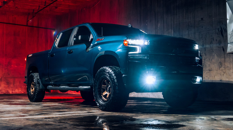 A blue Chevy Silverado shot at night with its headlights on.