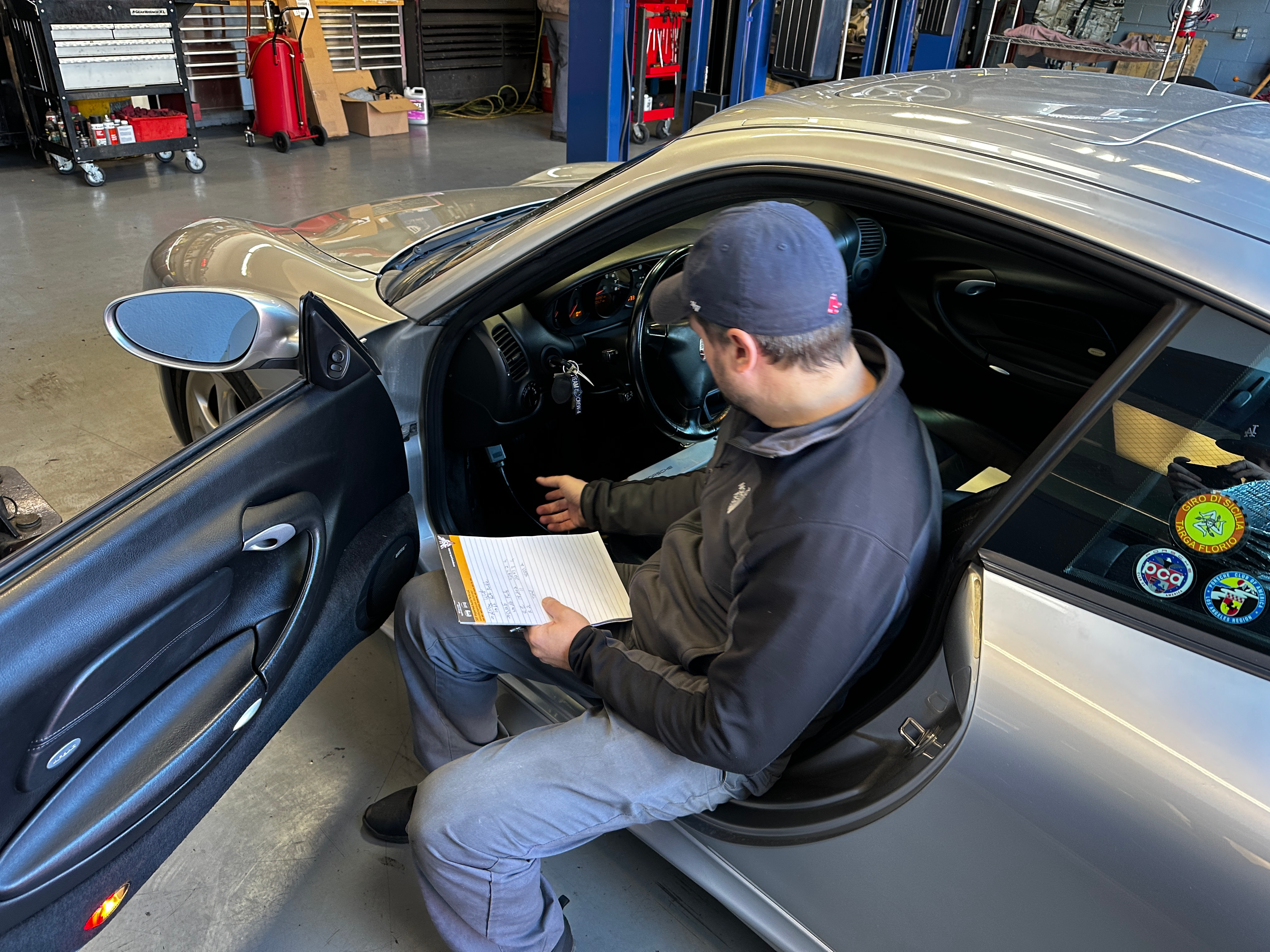 A man in a Boston Red Sox hat looks at a computer screen inside a 2001 Porsche 911.