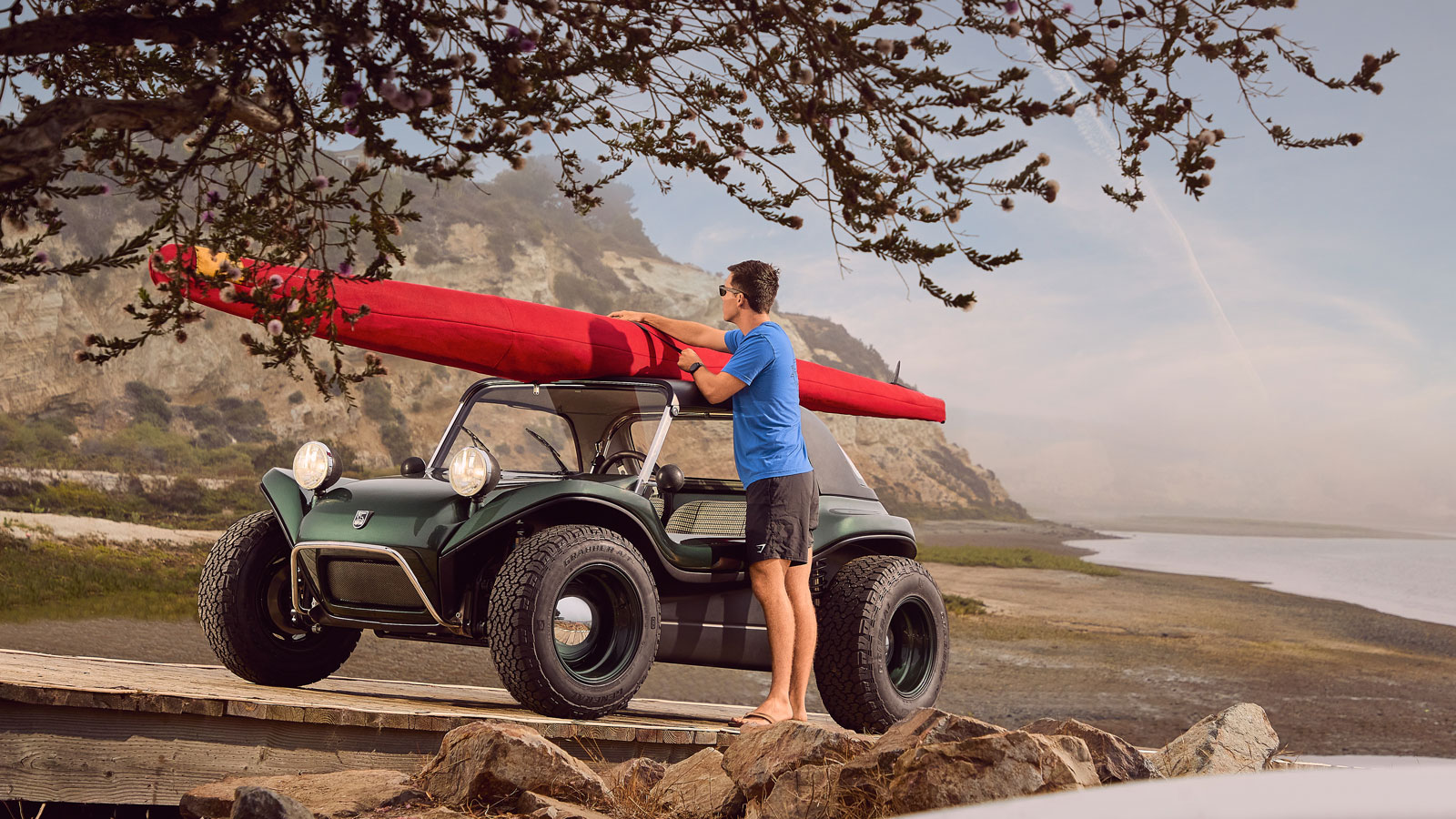 A photo of someone strapping a sea kayak to the roof of a dune buggy. 