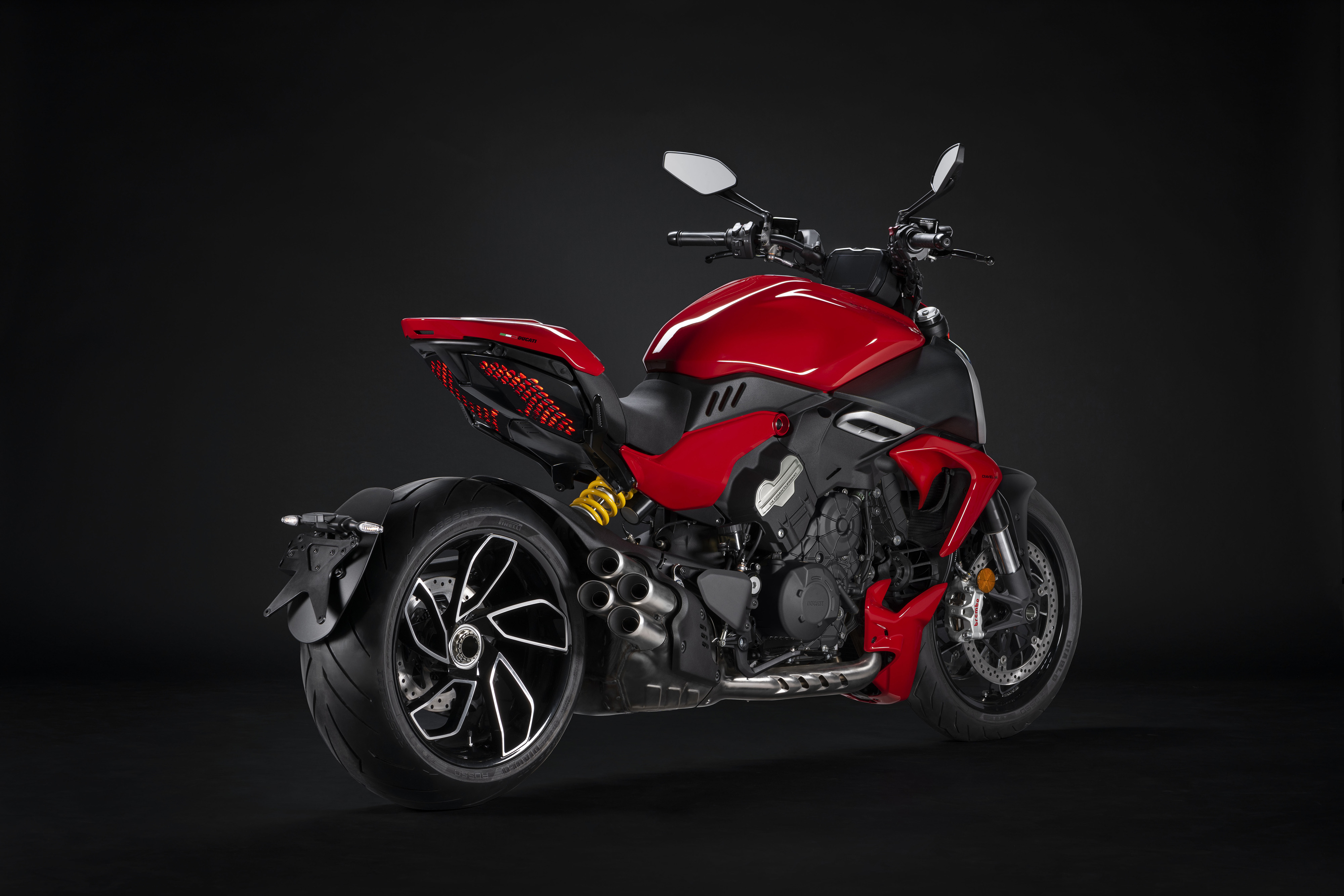 A red Ducati Diavel V4 parked in front of a black background, rear three-quarter view.