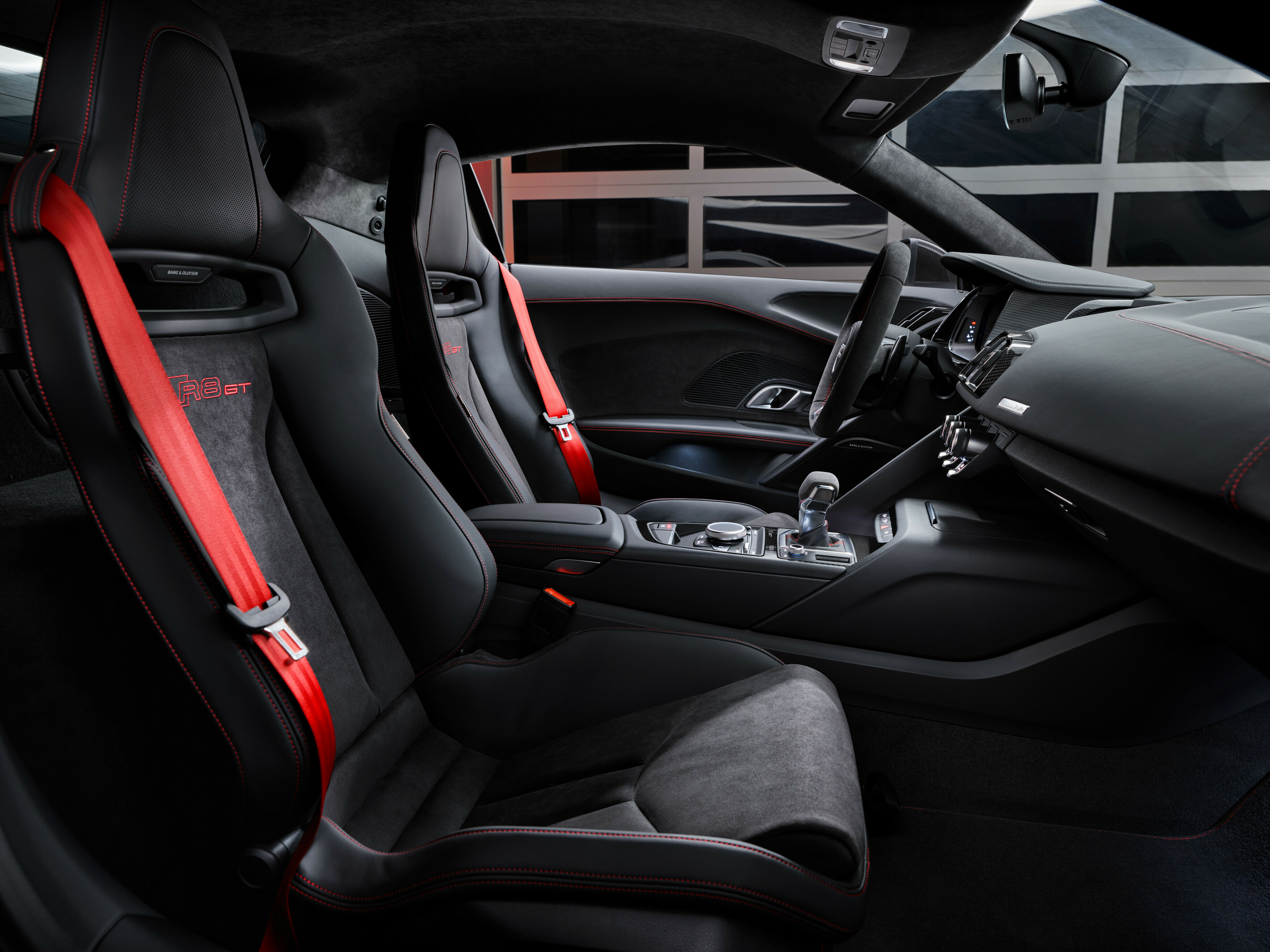 the interior of the 2023 audi r8 gt, upholstered entirely in black leather with red seat belts and red stitching on the seats that spells out 'r8 gt'