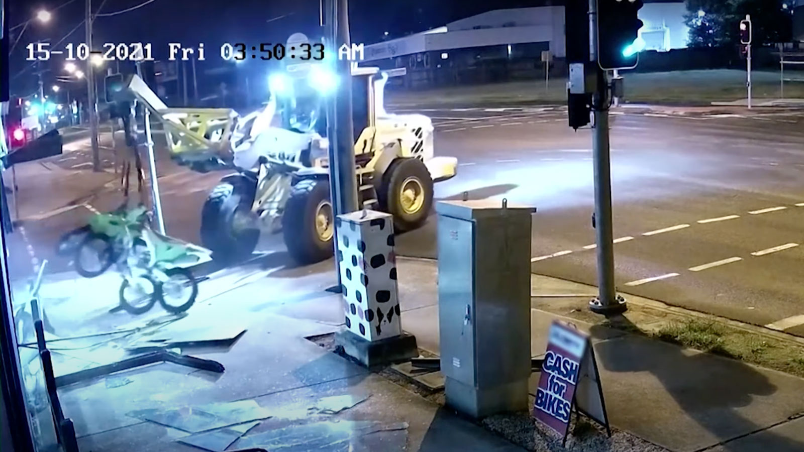 A yellow tractor pulls two motorbikes out the window of a dealership 