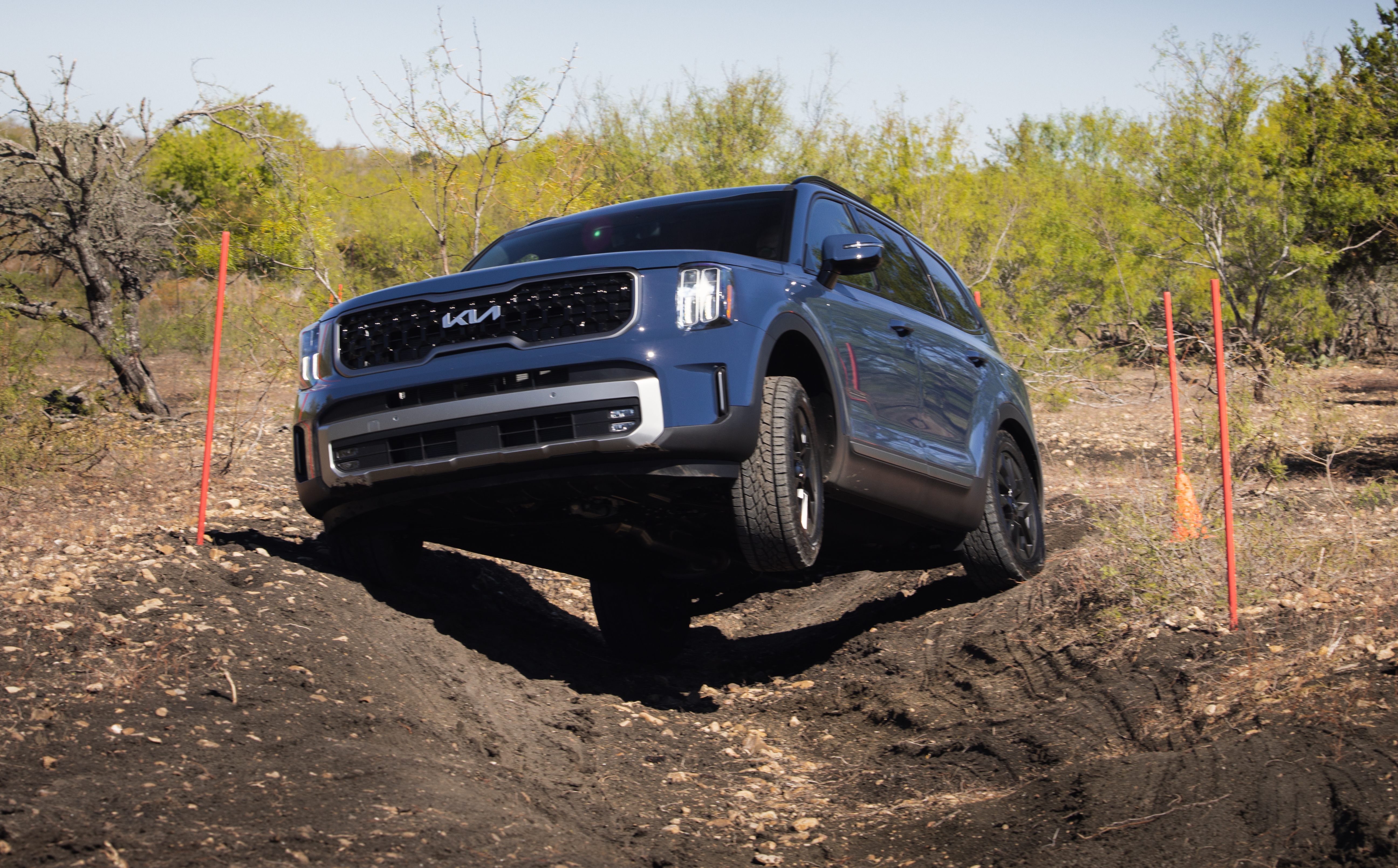 Blue 2023 Kia Telluride SX X-Pro on an off-road course, with its left front wheel in the air as it crawls out of a ditch.