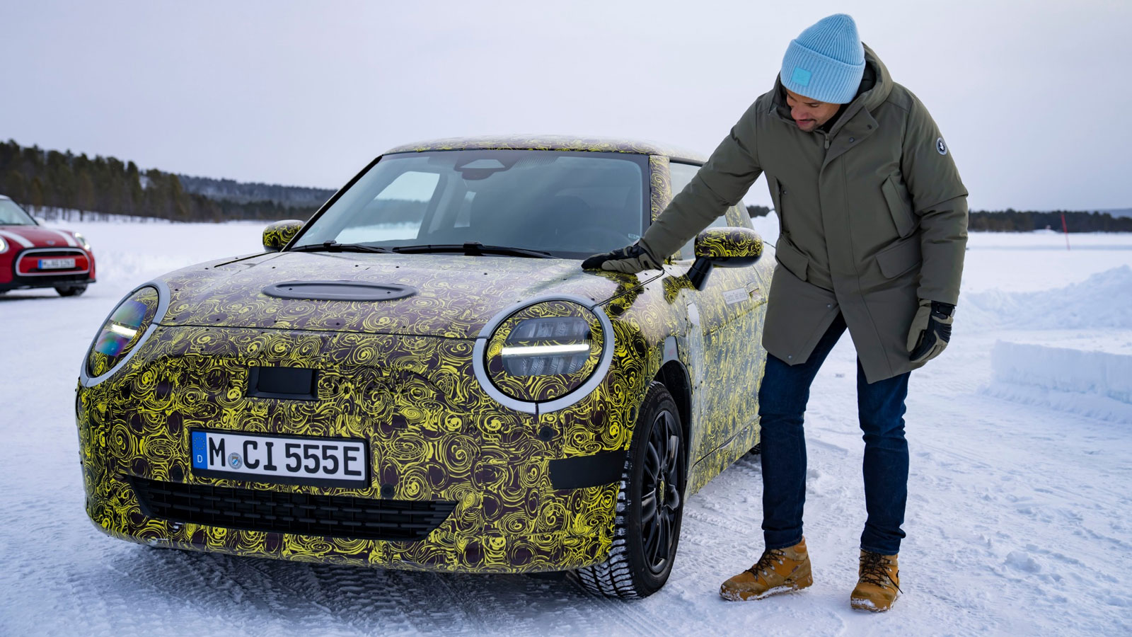 A photo of Mini head of design Oliver Heilmer patting the front of a camouflage test car. 