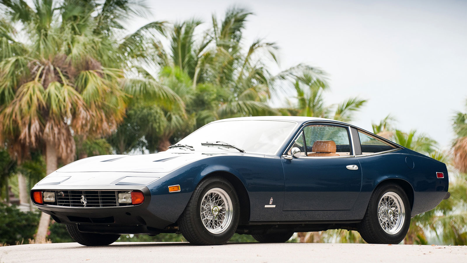 A photo of a vintage blue Ferrari parked by palm trees