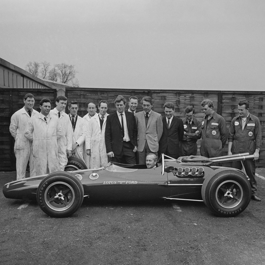 A photo of the Lotus team standing around a vintage car. 