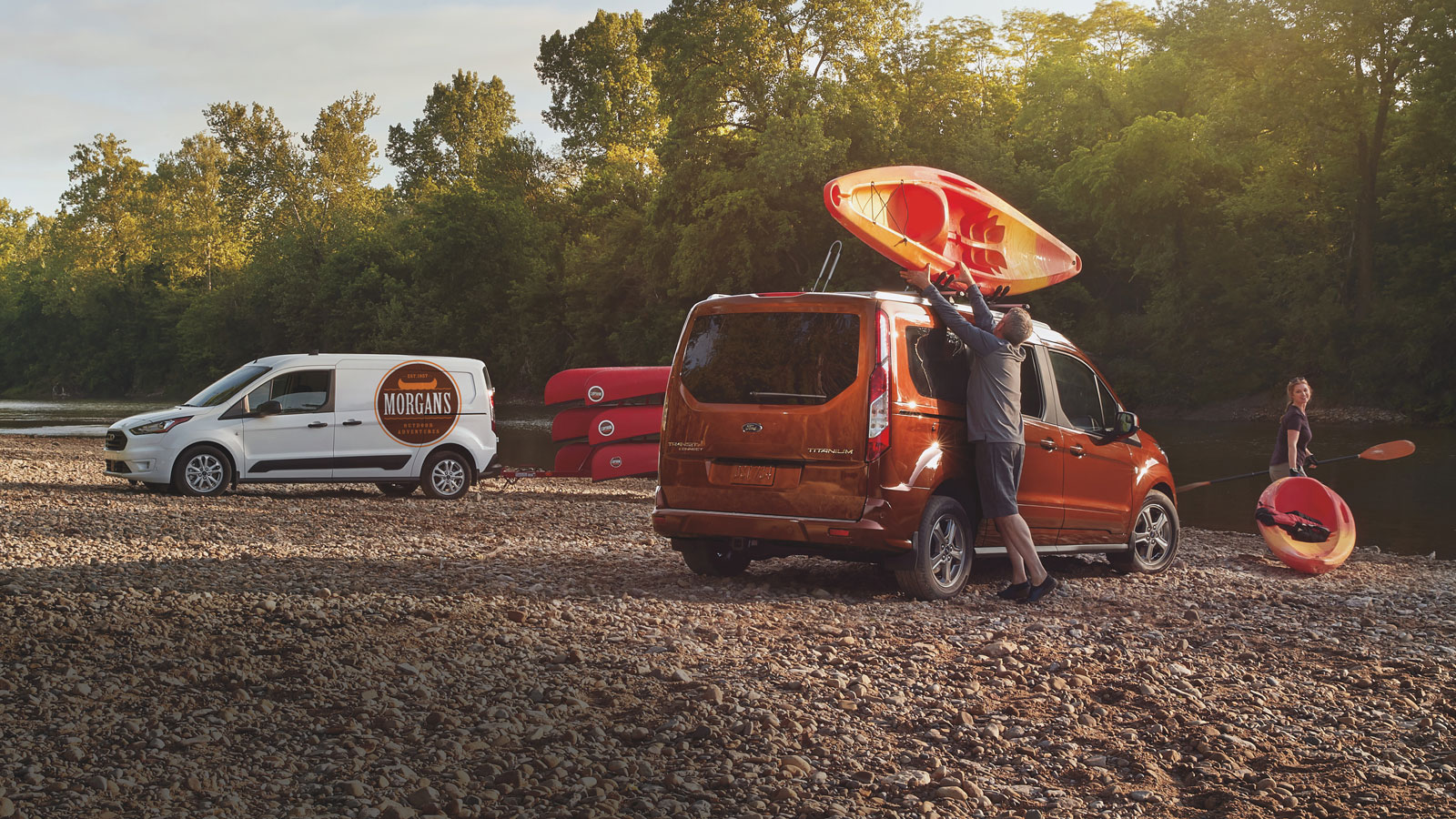 A photo of someone taking a kayak off the roof of an orange Transit Connect van. 