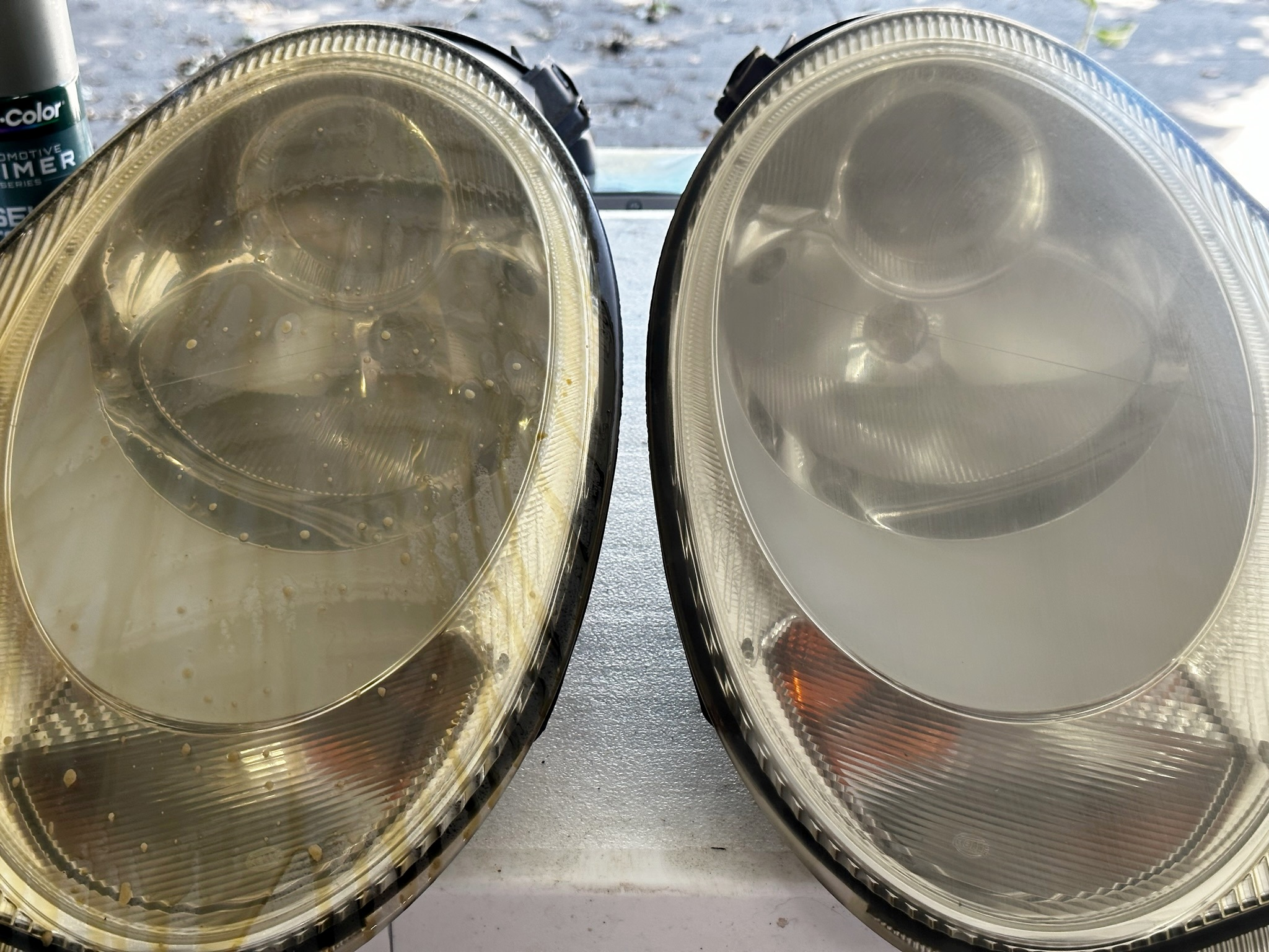 Two headlights on a table, one is dripping with brownish liquid, the other is hazy.