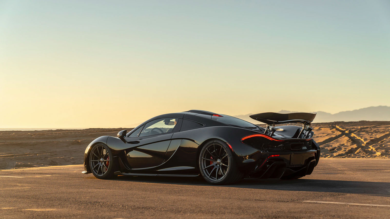 A black McLaren P1 in a parking lot at sunset 