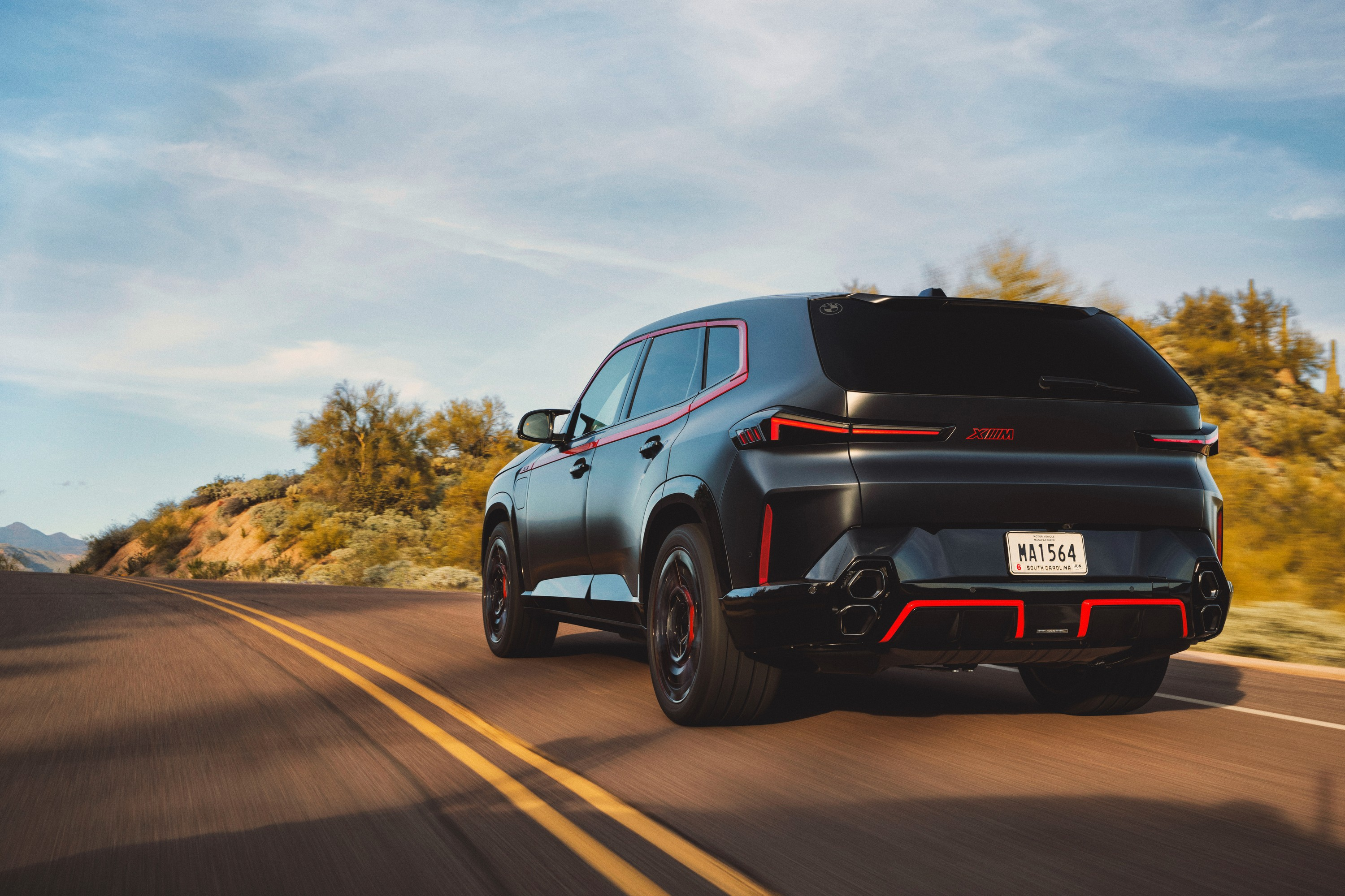 The rear three-quarter view of a black 2024 BMW XM Label Red driving in the desert