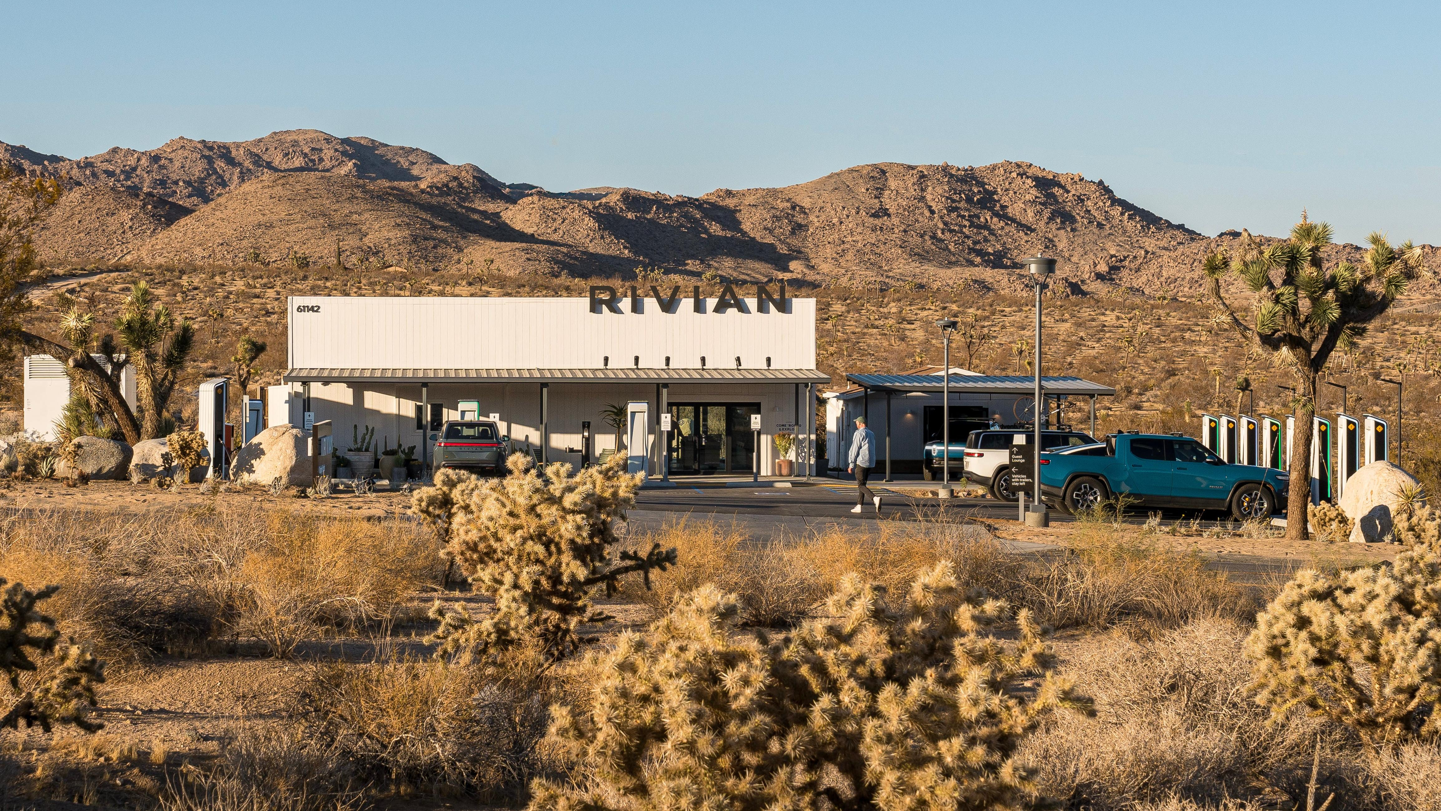 Another exterior shot of the Rivian Charging Outpost with JOshua trees in the foreground and mountains in the back