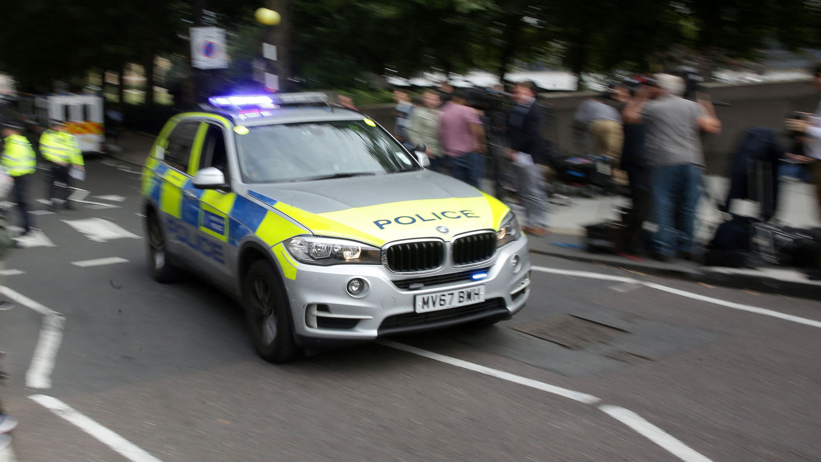 A police BMW X5 passes a crowd. 