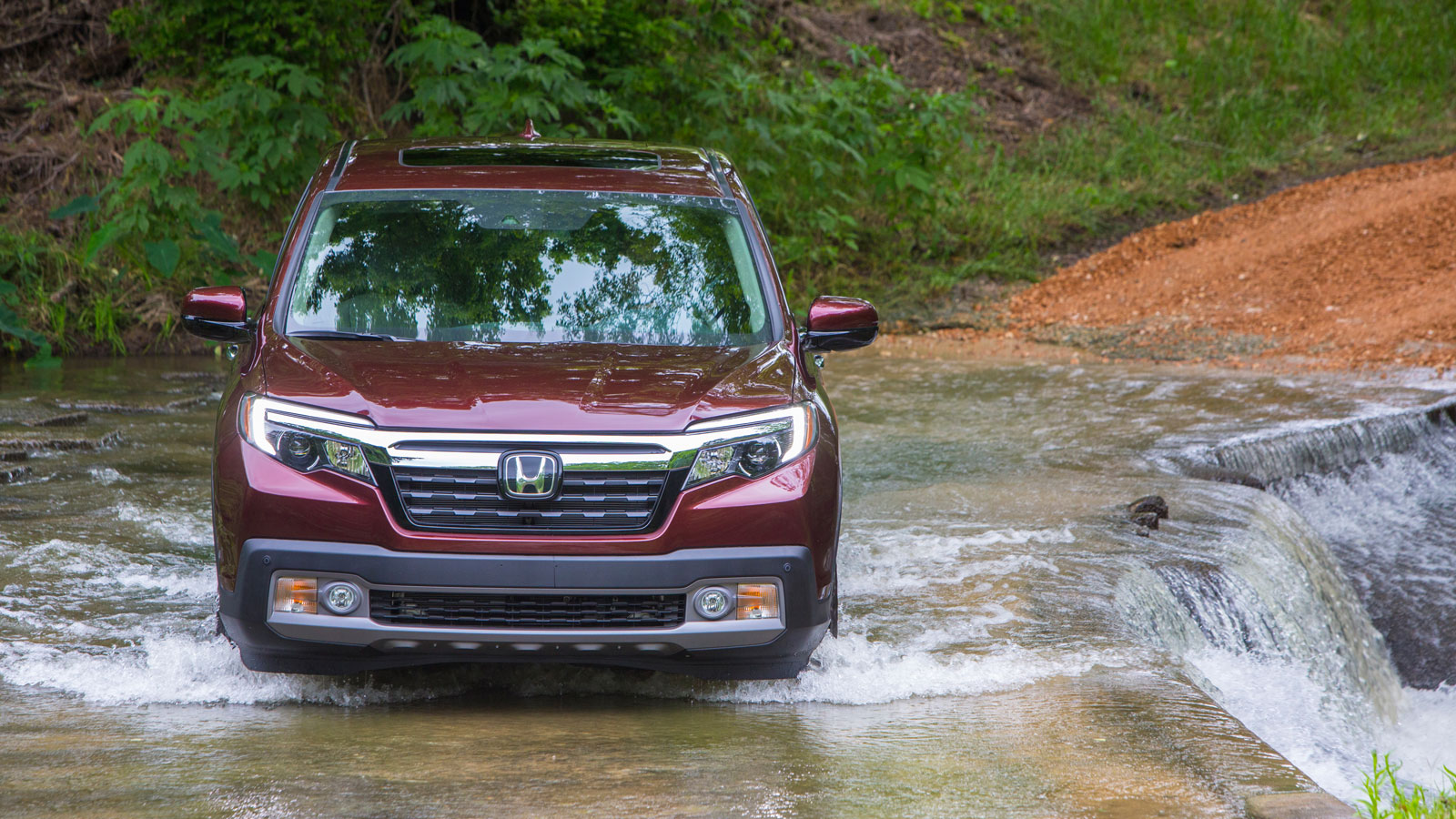 A photo of a Honda Ridgeline pickup truck driving through a stream. 