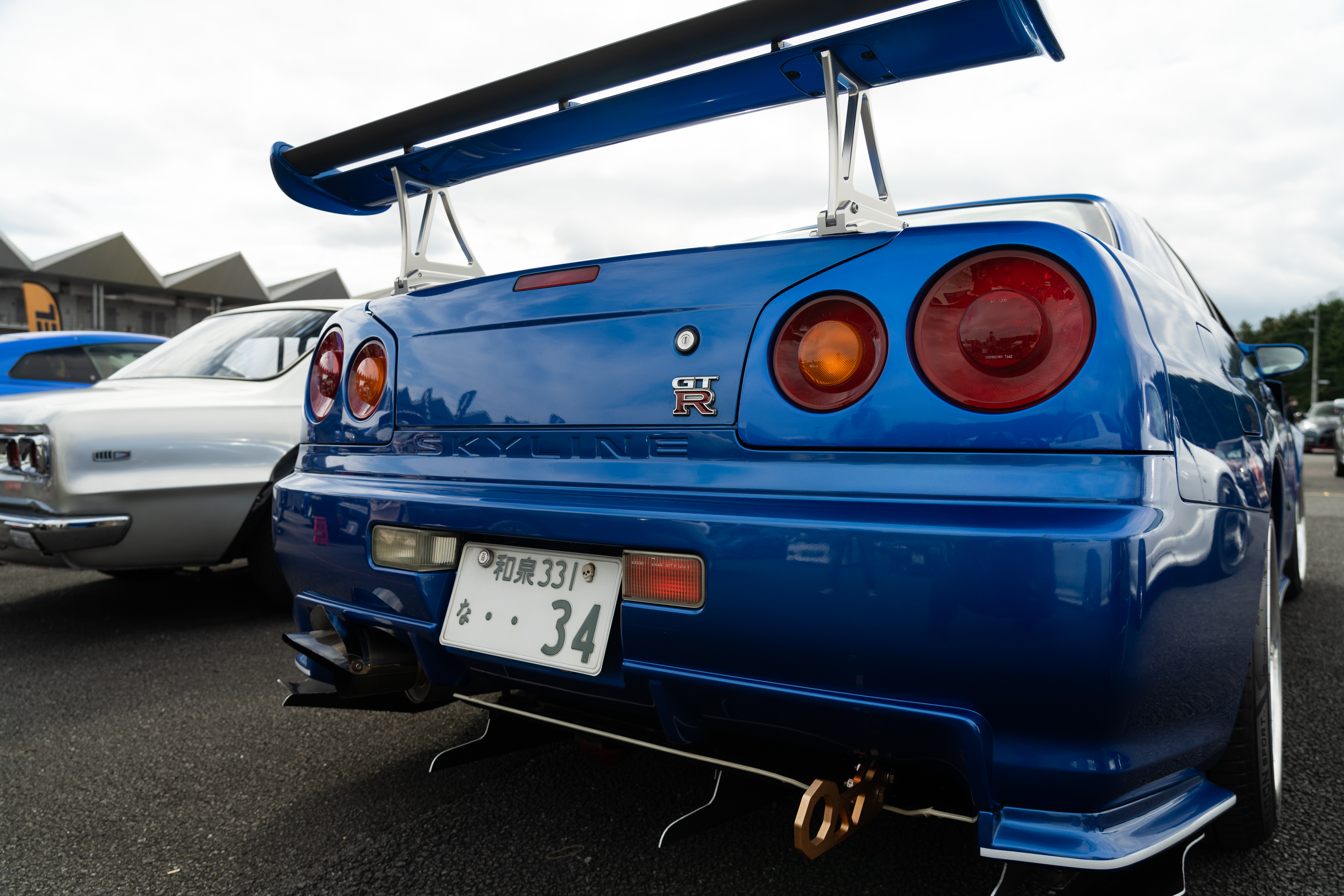 a close-up shot of the rear of an R34 nissan gt-r in blue, with a high wing on the trunk lid