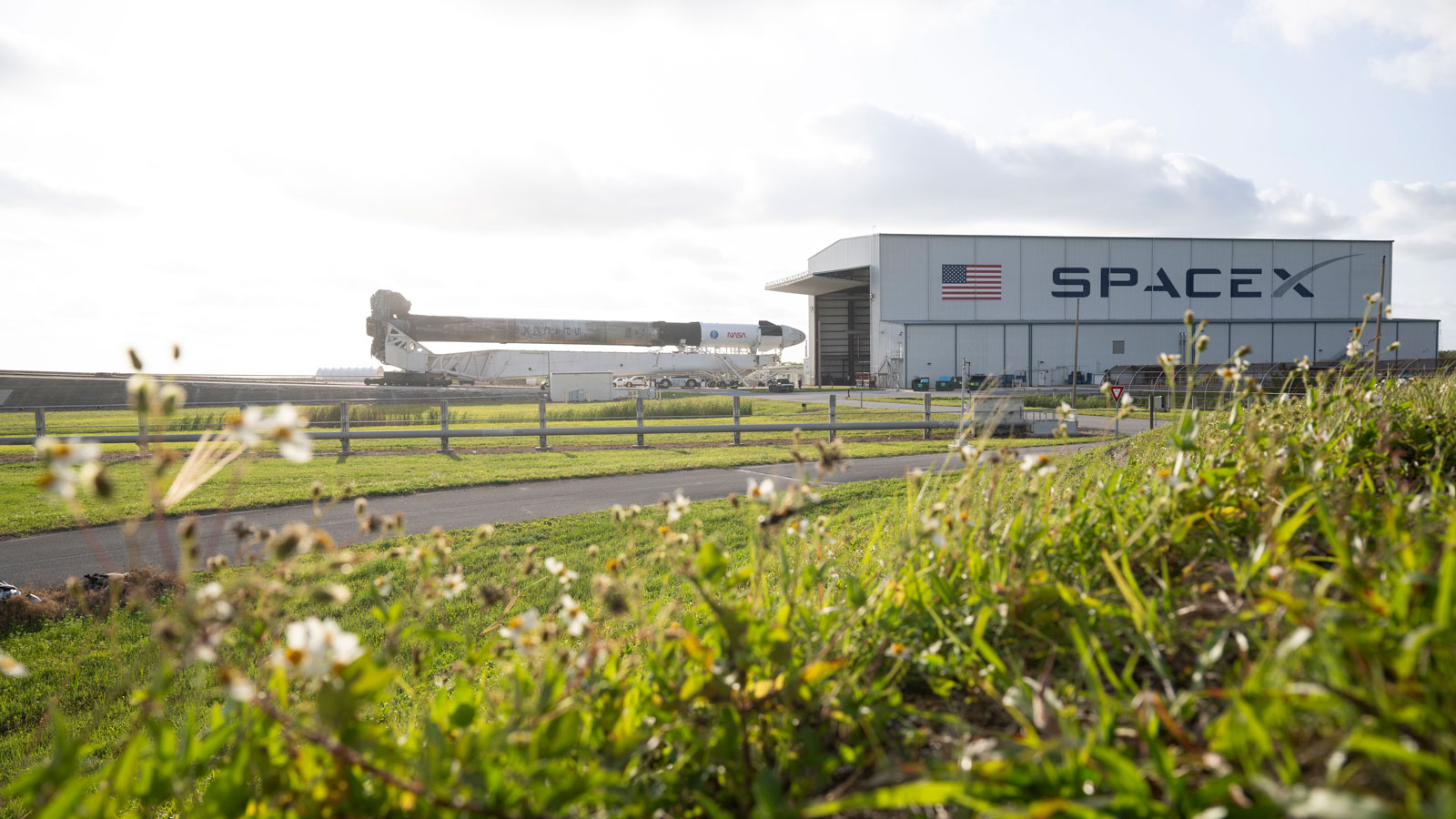 A photo of a SpaceX rocket laying on its side and rolling out of a hanger. 