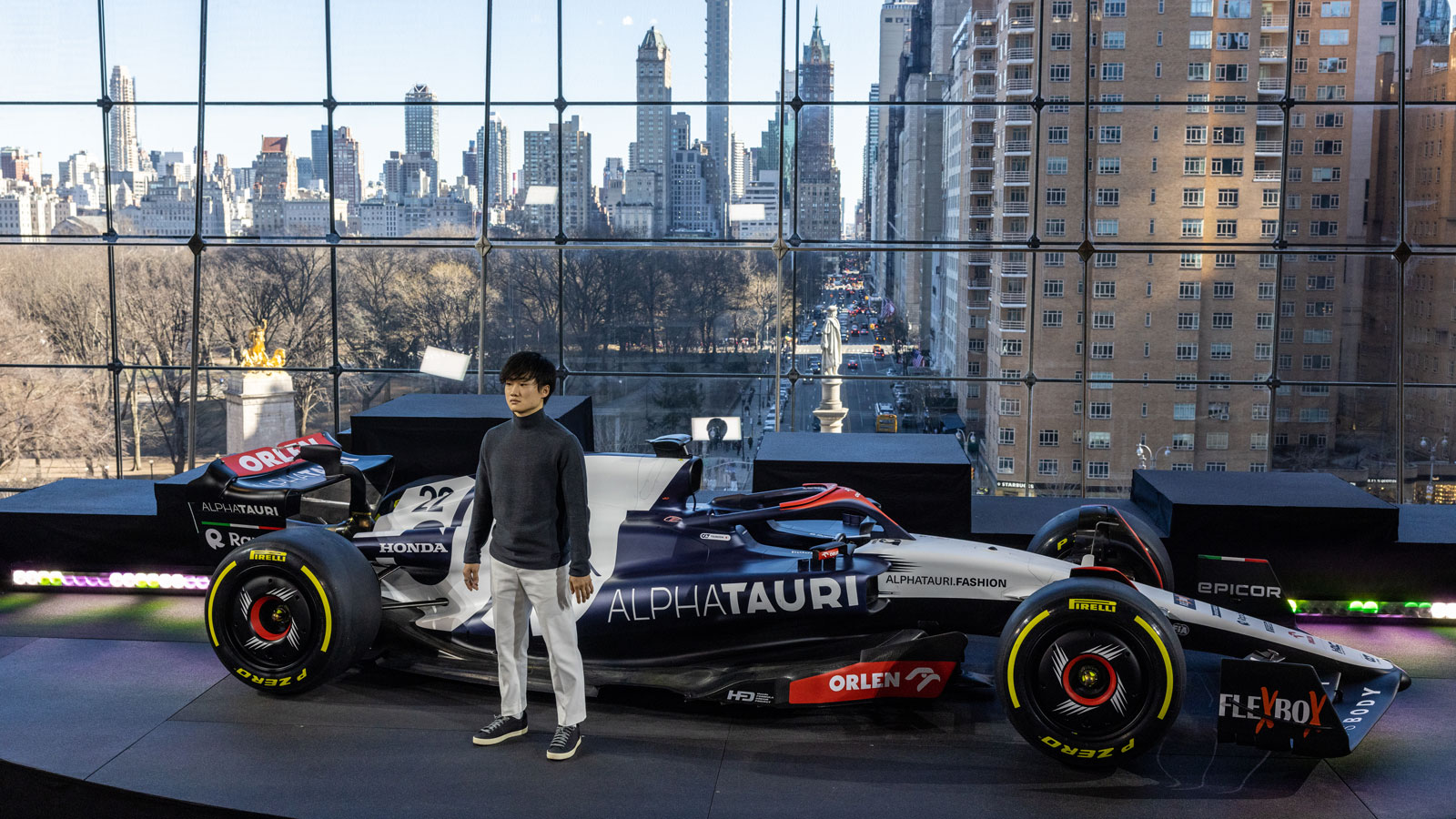 A photo of Yuki Tsunoda standing next to his 2023 AlphaTauri F1 car. 