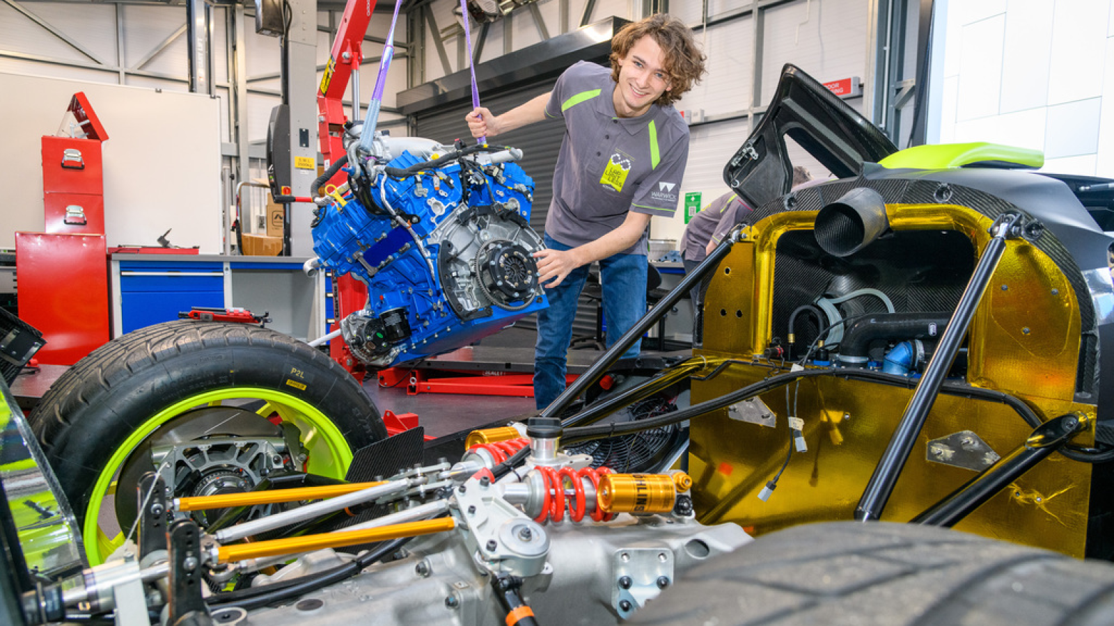 A photo of a student lifting the engine out a race car. 