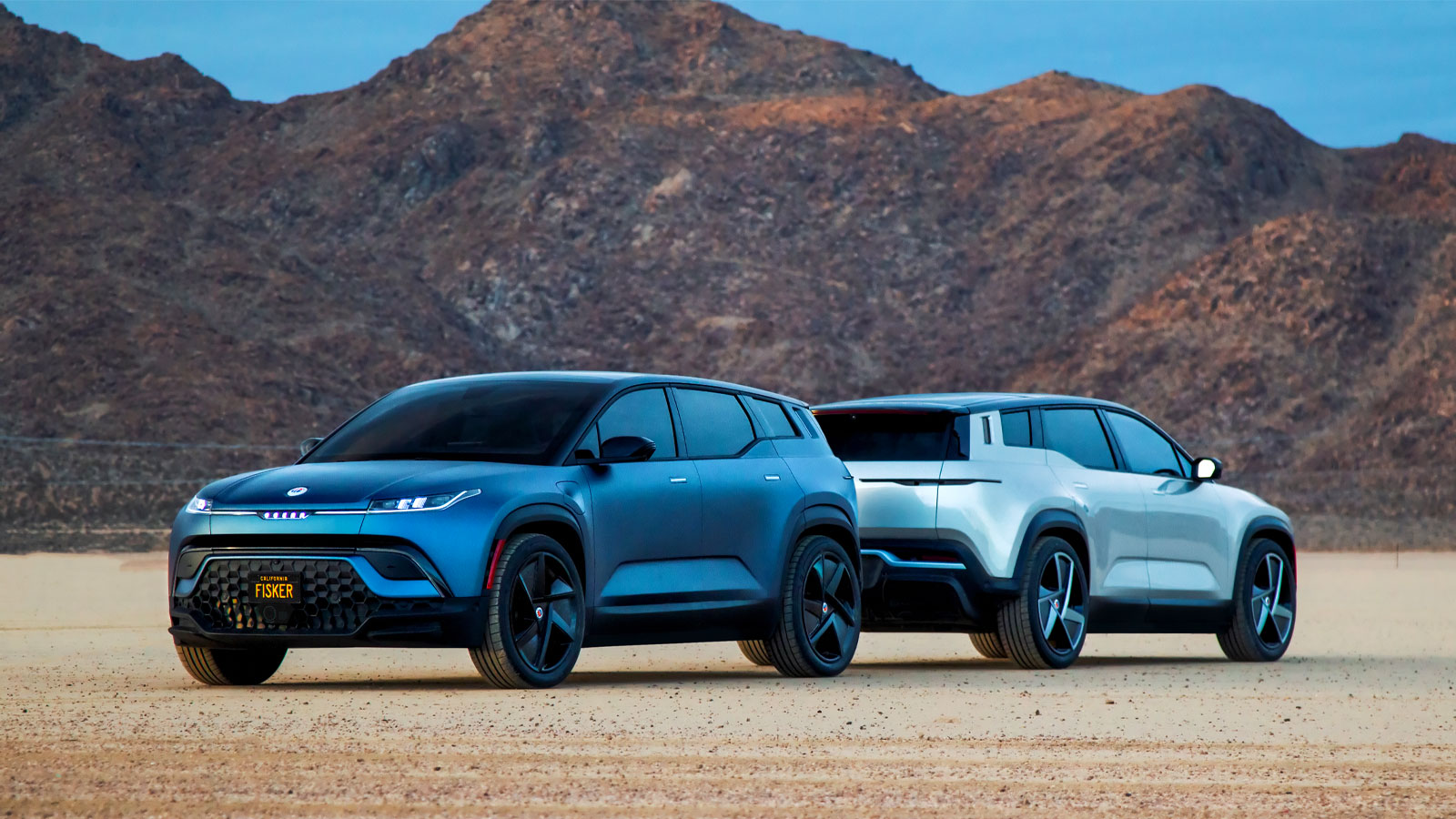 A photo of two Fisker Ocean electric SUVs parked back to back on sand. 